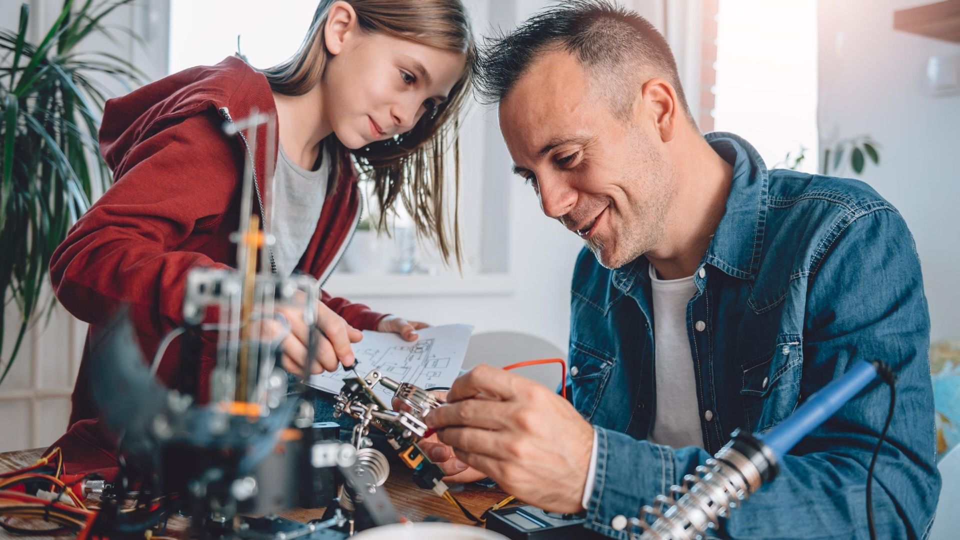 Un padre joven y su hija revisan el plano de un circuito mientras arman juntos un proyecto de electrónica