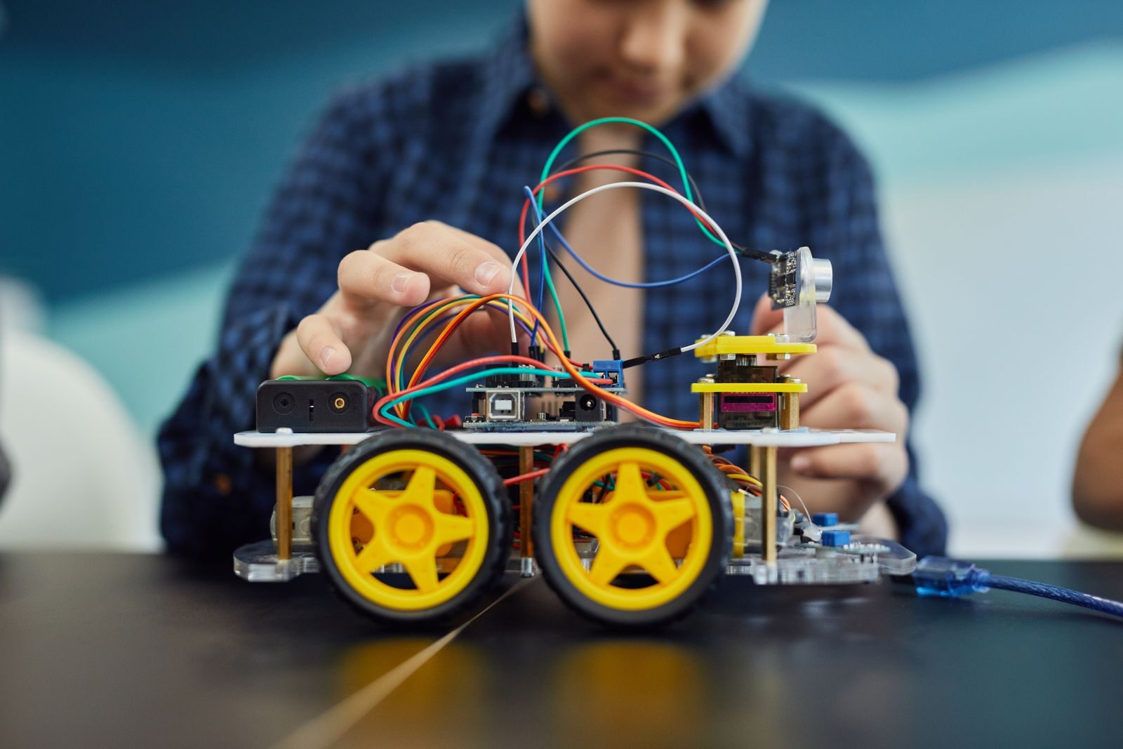 Las manos de un niño sobre un robot con ruedas y cables, ya armado